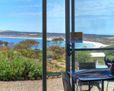 The scenic living room of Bayview Apartment at Emu Bay Holiday Homes, featuring a panoramic view of Emu Bay through large windows, complemented by cosy furnishings and warm lighting, providing guests with a comfortable and picturesque space to relax and unwind.