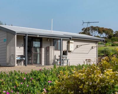 The exterior view of Cottage 3 at Emu Bay Holiday Homes, surrounded by lush greenery and bathed in natural light, providing a serene and picturesque setting for guests to enjoy their stay.