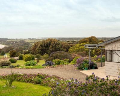 The exterior view of Jireh House, set amidst the picturesque landscape of Emu Bay Holiday Homes, featuring a charming facade framed by vibrant flora, providing a serene escape for guests.