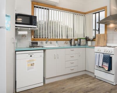 A modern and well-equipped kitchen inside Jireh House at Emu Bay Holiday Homes, featuring stainless steel appliances, ample counter space, and tasteful decor, providing a functional and stylish environment for cooking and dining.
