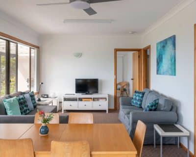 A cosy living room inside Jireh House at Emu Bay Holiday Homes, featuring comfortable seating, a fireplace, and large windows offering views of the surrounding natural beauty, inviting guests to unwind in comfort.