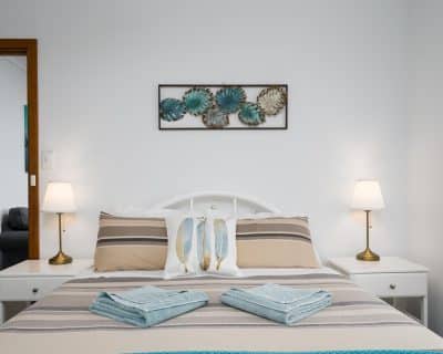 A tranquil bedroom inside Jireh House at Emu Bay Holiday Homes, adorned with soft bedding, warm lighting, and elegant furnishings, providing a peaceful retreat for guests to rest and recharge amidst the serene ambiance.