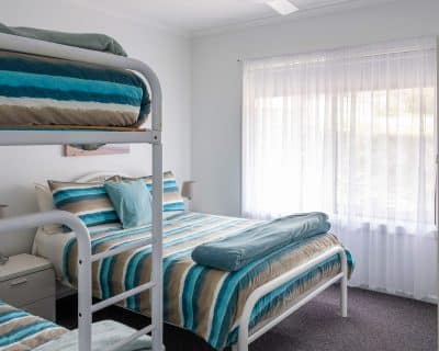 A cosy bedroom at Shalom House within Emu Bay Holiday Homes, featuring a comfortable bed, soft bedding, and large windows allowing natural light to fill the space, creating a peaceful atmosphere for rest and relaxation.