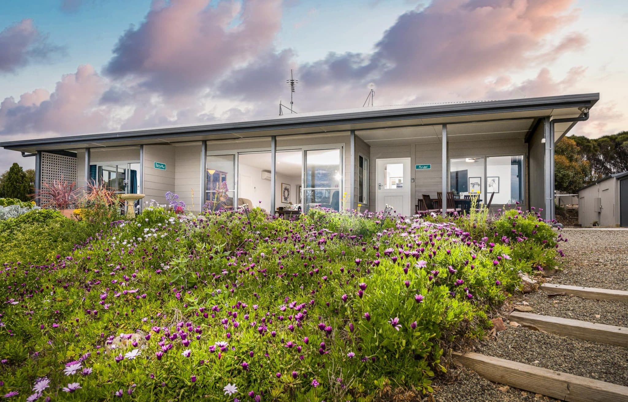Elegant front view of Amani House at Emu Bay, Kangaroo Island, designed to accommodate 2-9 guests. This beautifully renovated home boasts expansive sliding doors that frame stunning vistas from its elevated position. The property is equipped with a modern kitchen and a new, fully accessible second bathroom, making it ideal for a relaxing getaway.